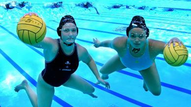 Two women playing water polo underwater 