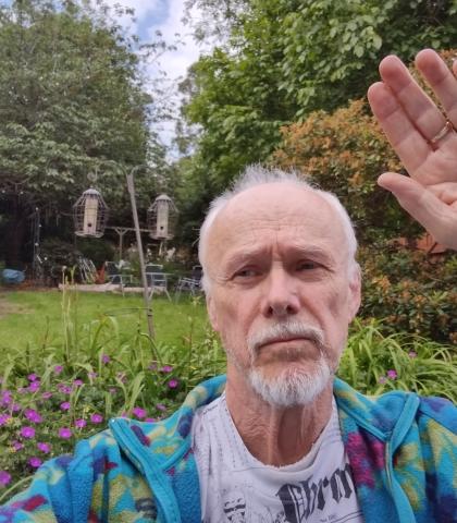 Landscape image of Tony raising his hand with a garden in the background