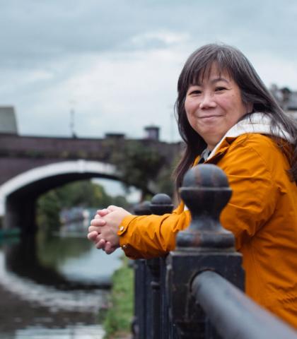 A woman smiling at the camera, leaning against a barrier next to a canal