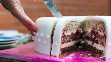 A white iced cake being cut into slim portions by a hand holding a cake knife. 