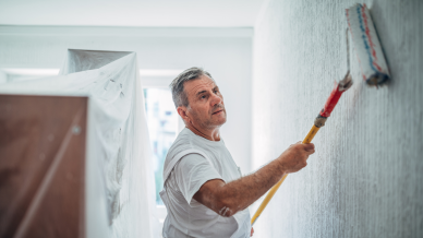 A man dressed in white overalls painting a white wall using a paint roller.