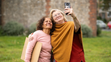 two older women taking a selfie on a mobile phone outdoors after a class